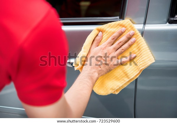 Male auto care service staff cleaning car door with\
microfiber cloth