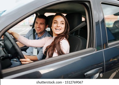 Male auto instructor takes exam in young woman. Cheerful attractive female driver posing at driver's place. Look from car. Hold hands on sheering wheel. - Powered by Shutterstock