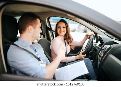 Male auto instructor takes exam in young woman. Practical issue. Cheerful happy and positive student look at teacher and smile.