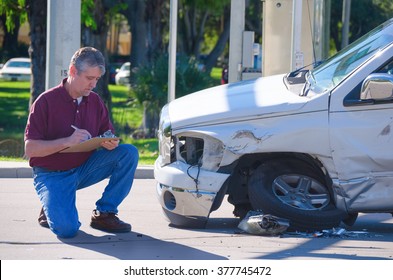 Male Auto Insurance Adjuster Inspecting A Vehicle That Has Been In An Accident Wreck