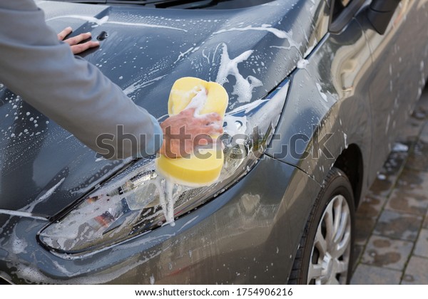 Male\
auto service staff washing a car bonnet with\
sponge
