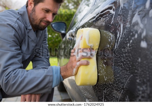 Male\
auto service staff washing a car roof with\
sponge