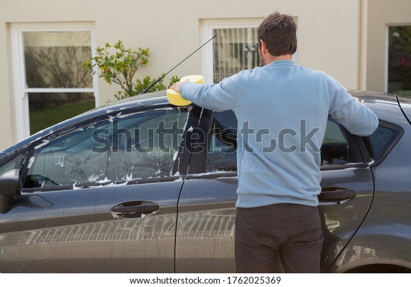 Male\
auto service staff washing a car roof with\
sponge