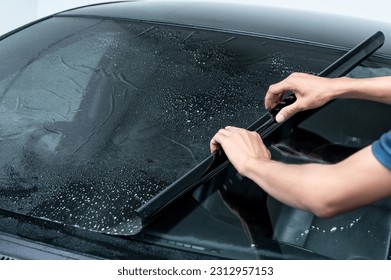 Male auto specialist worker hand rolling car window film on front windscreen glass surface. Car side window film removal and tinting installation. 