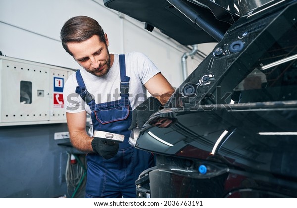 Male automotive technician peening car part\
during auto service
