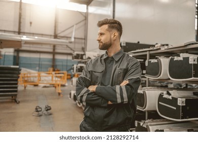 Male aviation maintenance technician keeping arms crossed and looking away while standing in aircraft repair station