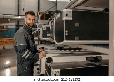 Male Aviation Maintenance Technician Looking At Camera And Smiling While Standing In Aircraft Repair Station