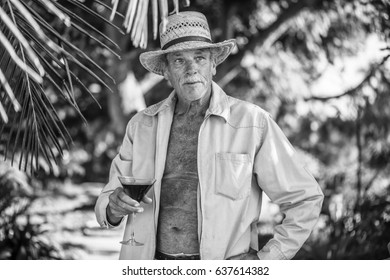 Male Baby Boomer In Straw Hat Enjoying A Cocktail In A Tropical Location, Black And White Photo; Retirement, Vacation
