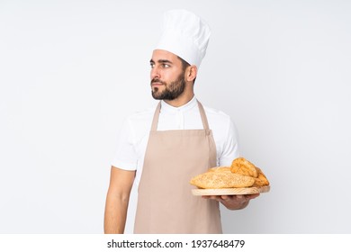 Male Baker Holding A Table With Several Breads Isolated On White Background Looking Side