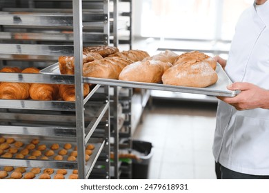 Male baker holding a tray of baked breads in bakery shop. - Powered by Shutterstock