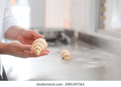 A male baker makes croissants in the bakery kitchen. - Powered by Shutterstock