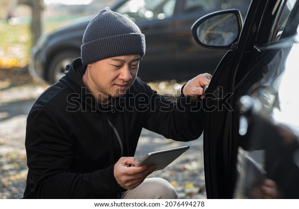 male bandit thief car thief asian uses a tablet to
turn off the car alarm