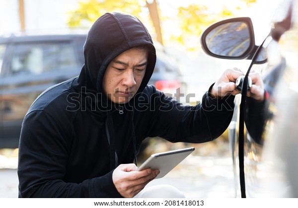 male bandit thief car thief asian uses a tablet to\
turn off the car alarm