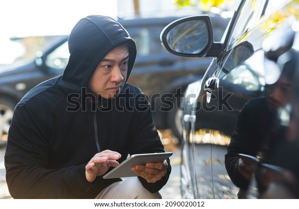 male bandit thief car thief asian uses a tablet to\
turn off the car alarm