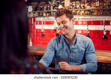 Male Bar Tender Standing Behind Counter Serving Drinks To Customer