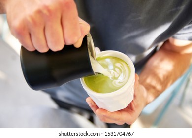 Male Barista Making Vegan Matcha Cappuccino With Oat Milk With Latte Art In Outdoor Cafe.