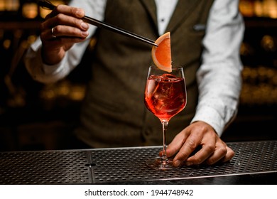 male bartender accurate holding tweezers with citrus slice over wine glass with bright cold iced cocktail - Powered by Shutterstock