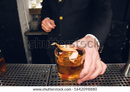 Male bartender or barman offering an alcohol beverage, cocktail or drink on the rocks, in bar, nightclub, restaurant or pub