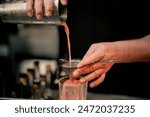 a male bartender pouring a alcoholic drink from the steel shaker to the glass through the sieve on the bar counter