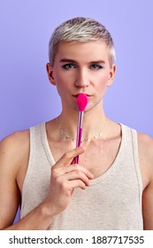 Male Beauty Blogger Holding Make-up Brush Near Mouth And Looking At Camera Isolated On Purple Background