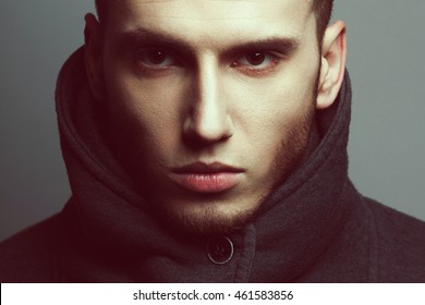 Male beauty concept. Portrait of brutal young man with short hair wearing gray sweatshirt with high collar and buttons posing over gray background. Modern street style. Close up. Studio shot