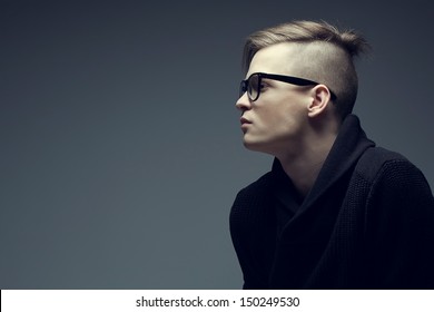 Male Beauty Concept. Portrait Of Fashionable Young Man With Stylish Haircut Wearing Trendy Glasses And Sweater, Posing Over Gray Background. Perfect Hair & Skin. Hipster Style. Copy-space. Studio Shot