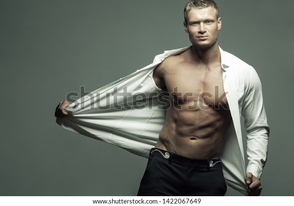男性の美しさ ファッションコンセプト グレイの背景にポーズをとるズボン クラシックシャツの筋肉質の男性モデルのハンサムなポートレート 自分の体を見せてる 男 金髪 健康に清潔な肌 スペースのコピー の写真素材 今すぐ編集