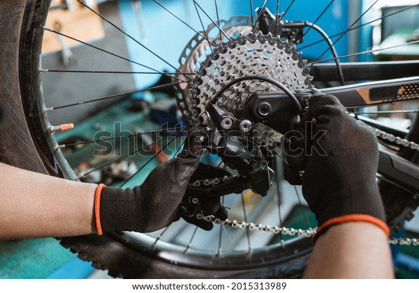 male bicycle\
mechanic\'s hand in gloves attaches chain over rear derailleur and\
sprocket in workshop