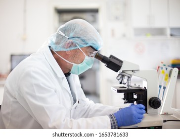 Male Biologist Testing Samples In Laboratory, Looking Through Microscope