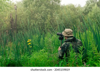 male birdwatcher makes observations in the wild with a spotting scope standing among the tall grass - Shutterstock ID 2045159819