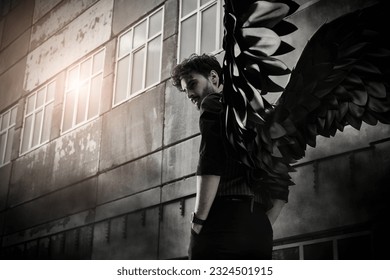 A male Black Angel stands at sunset in front of an old concrete building. Place for text. The concept of war, doomsday, Apocalypse. - Shutterstock ID 2324501915