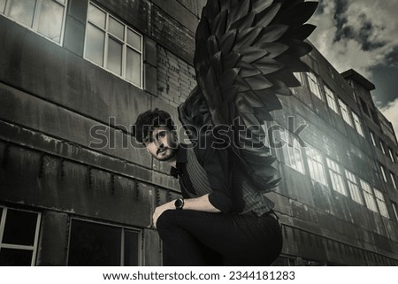 A male Black Angel stands at sunset in front of an old concrete building. Place for text. The concept of war, doomsday, Apocalypse.