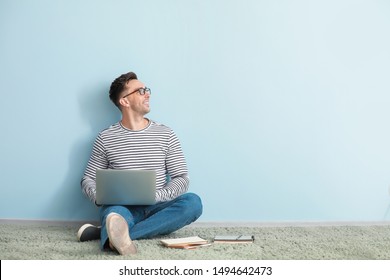 Male blogger with laptop sitting near color wall