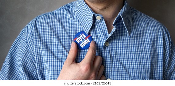 A Male In Blue And White Shirt Holding A Button Pin Encouraging Viewer To Cast Your Ballot