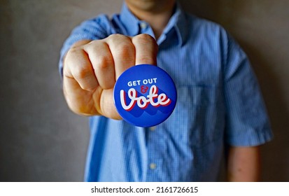 A male in blue and white shirt holding a button pin encouraging viewer to cast your ballot