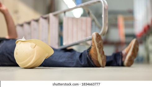 Male Body Lying On The Floor After A Work Accident. Fallen Ladder And Safety Helmet Lying Next To The Body.