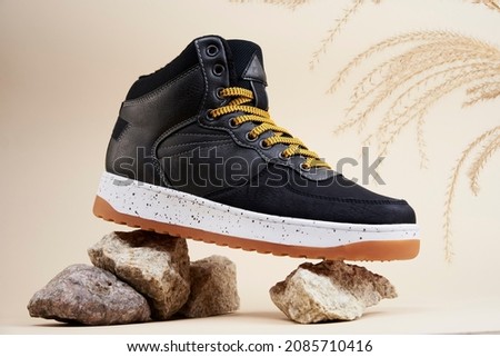 Male boots on beige background. Winter stylish leather shoes on stones with dried plant