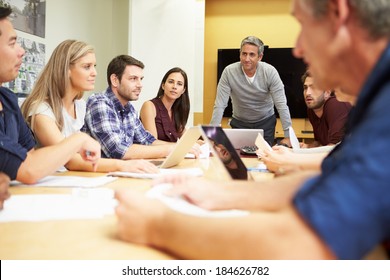 Male Boss Addressing Meeting Around Boardroom Table