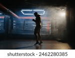 A male boxer is boxing with a shadow on the background of a boxing ring. A boxer practices his punches in a boxing studio.