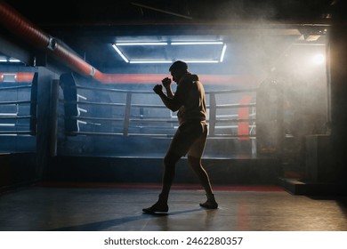 A male boxer is boxing with a shadow on the background of a boxing ring. A boxer practices his punches in a boxing studio. - Powered by Shutterstock