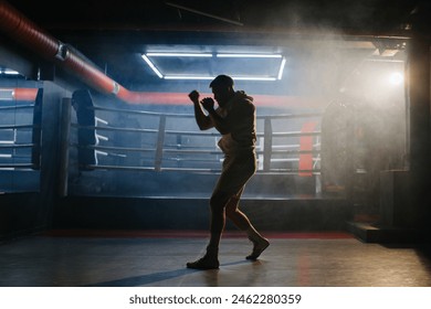 A male boxer is boxing with a shadow on the background of a boxing ring. A boxer practices his punches in a boxing studio. - Powered by Shutterstock