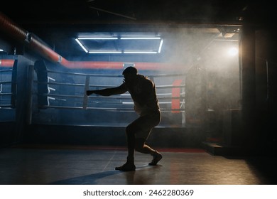 A male boxer is boxing with a shadow on the background of a boxing ring. A boxer practices his punches in a boxing studio. - Powered by Shutterstock