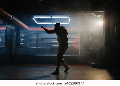 A male boxer is boxing with a shadow on the background of a boxing ring. A boxer practices his punches in a boxing studio. - Powered by Shutterstock