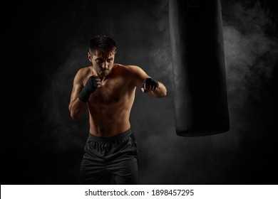 Male boxer training defense and attacks in boxing bag on black background - Powered by Shutterstock