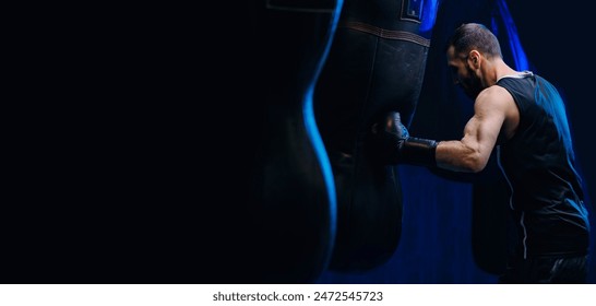 Male boxer trains punches on punching bag, dark background. Concept banner sport boxing. - Powered by Shutterstock