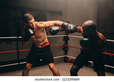 Male Boxers Throwing Punches At Each Other During A Fight In A Boxing Ring. Two Athletic Young Men Having A Boxing Match In A Fitness Gym.