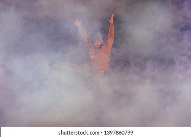 Male breakdancer jumps off high in the air while performing a cool dance move, a lot of smoke in the background. - Powered by Shutterstock