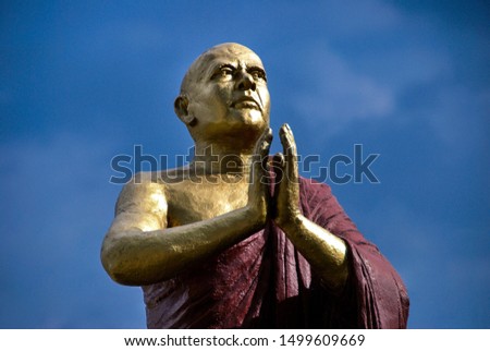 Male bronze sculpture of a monk, who prays to the Buddha, against a blue sky