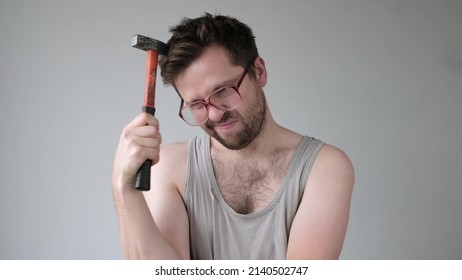 Male builder in big glasses scratches his head with a hammer. I do not know how to repair it. - Shutterstock ID 2140502747