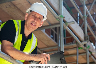 Male Builder Foreman, Construction Worker Or Site Manager Holding A Clipboard, Wearing A White Hard Hat And Hi Vis Vest